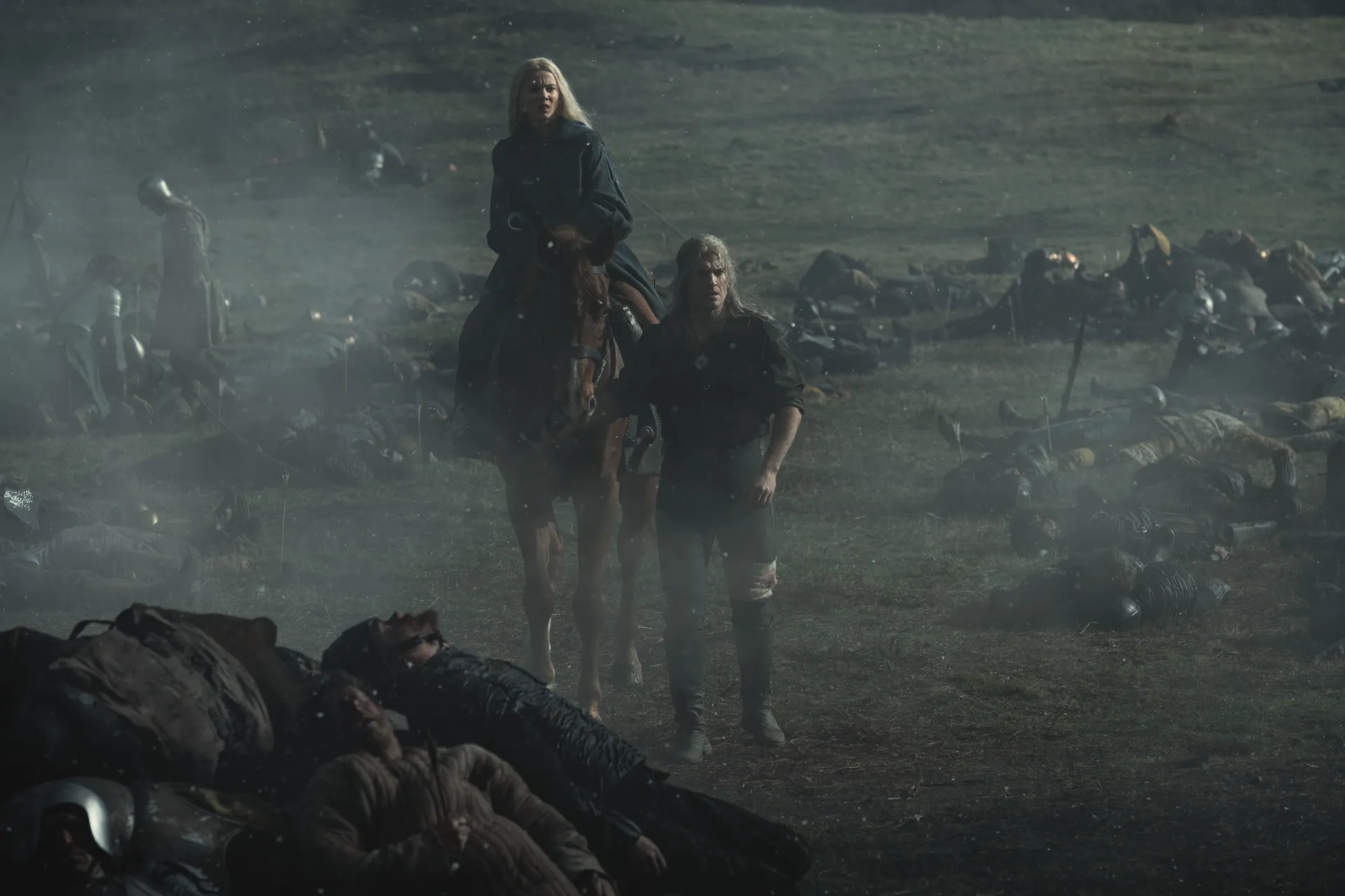 Geralt leder sin häst till fots medan Ciri rider genom ett slagfält i Netflix The Witcher.